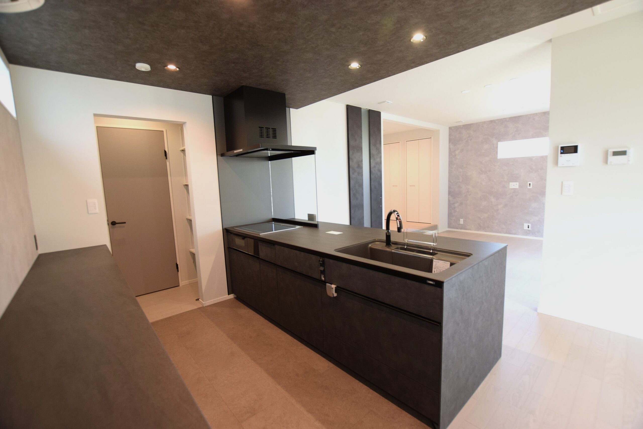 リビング・ダイニングと緩やかにつながるペニンシュラ型キッチン。<br/>
開放感があり、家族との会話も楽しみながら家事ができます。<br/>
モノトーンでまとめ、空間全体の統一感も大切にしました。<br/><br/>

キッチン部分床：クルードフローリング【ピエトラグレー】<br/>
建具：シンプルライン【Pグレー】